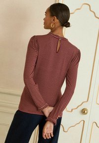 Svītrains garroku tops bordīna un krēmkrāsā ar atslēgas caurumu mugurpusē un volānveida aprocēm. Mīksts audums ar pieguļošu siluetu.