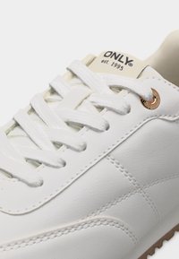 Λευκό δερμάτινο αθλητικό παπούτσι με λευκά κορδόνια, λεπτομερείς ραφές και μπεζ γλώσσα με την επιγραφή "ONLY est. 1995."