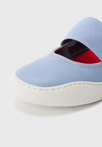 Zapato de cuero azul claro con suela de goma blanca, con una ancha banda de tela azul y forro interior rojo. Textura suave y forma redondeada.