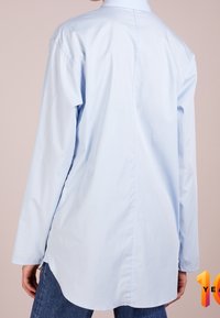 Light blue long-sleeve shirt made of cotton, featuring a classic collar, curved hem, and a relaxed fit, view from the back.