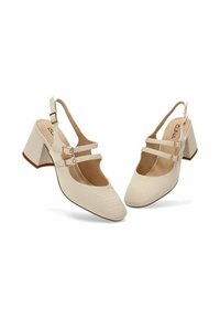 Zapatos de tacón tipo slingback en color beige, con un patrón de cocodrilo texturizado, dos correas ajustables en el tobillo con hebillas metálicas y un diseño de tacón cuadrado.