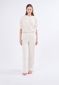 Conjunto de loungewear de punto en un tono beige claro que presenta una textura acanalada, un suéter de corte relajado con mangas caídas y pantalones de pierna ancha con cinturilla elástica.
