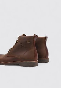 Botas de cuero marrón hasta el tobillo con una textura suave, punta redonda, diseño de cordones y suela de goma. Presenta grabado de logo y costuras en contraste.