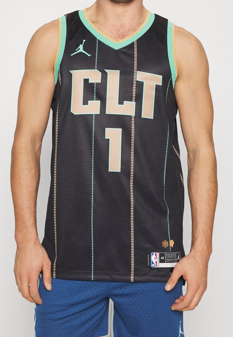 Homme portant un maillot de basketball noir avec des bordures turquoises, "CLT" et le numéro 1 sur le devant, associé à un short bleu avec de petites perforations.