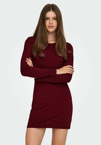 Vinröd klänning med lång ärm och figurnära silhuett, prydd med små silverprickar. Mjukt tyg med slät textur.