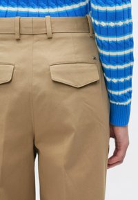 Μπεζ βαμβακερό παντελόνι με λείο υφή, με δύο πίσω τσέπες και εφαρμοστό ζωνάρι στη μέση. Ένα μπλε και άσπρο πουλόβερ με σχέδιο διακρίνεται μερικώς.