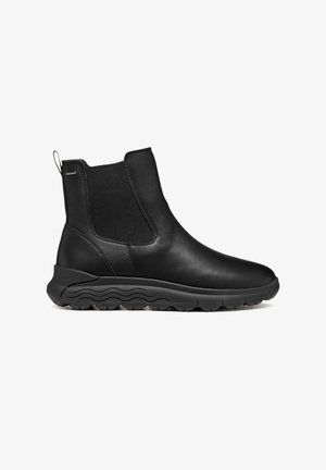 Botas de cuero negro hasta el tobillo con paneles elásticos laterales, puntera redondeada y suela de goma texturizada con un patrón en forma de ola. Con lengüeta en la parte posterior.