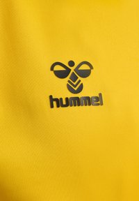 Tissu jaune avec un logo d'abeille stylisé noir et le texte "hummel" imprimé dessus.