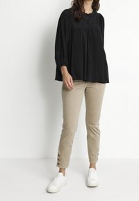 Svart plisserad topp med en strukturerad halsringning, kombinerad med beige figursydda byxor med knappdetaljer vid fållarna och vita sneakers.