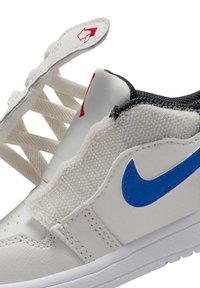 Λευκό αθλητικό παπούτσι με μπλε λογότυπο Nike, μαύρο πλεκτό κολάρο, επενδυμένη γλώσσα και μερικά αποσπασμένα κορδόνια που δείχνουν την εσωτερική κατασκευή.