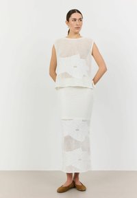 Set din două piese alb, tricotat, compus dintr-un top fără mâneci și o fustă lungă, ambele cu modele florale și un design din plasă texturată.
