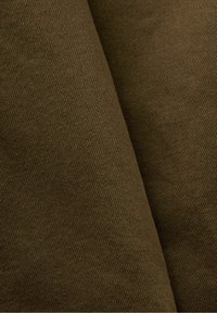 Tissu en coton marron à texture lisse, présentant un motif de tissage diagonal. Le matériau est plié, créant des courbes et des ombres.