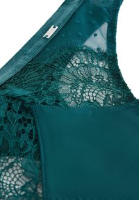 Teal spetsbh med genomskinligt mesh och detaljer. Har ett blommönstrat spetstygn på ena sidan, slät tyg på den andra sidan, och en silverklämma.