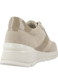 Zapatilla beige con detalles de ante y cuero charolado, punta redondeada, suela blanca gruesa, diseño perforado y logotipo en relieve en el talón.