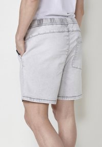 Shorts de mezclilla gris con cinturilla elástica, bolsillos laterales con abertura y un bolsillo trasero de parche. Corte recto con detalles de costura a contraste.