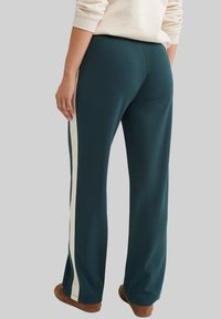 Turkosa vida sweatpants med en vit sidstripe, mjuk textur, detaljerad sömnad och en bekväm passform. Bärs med bruna tofflor.