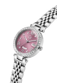 Sølvfarvet metalur med en lyserød urskive, romerske tal og diamanter som detaljer. Har et datovindue og et link-armbånd design.