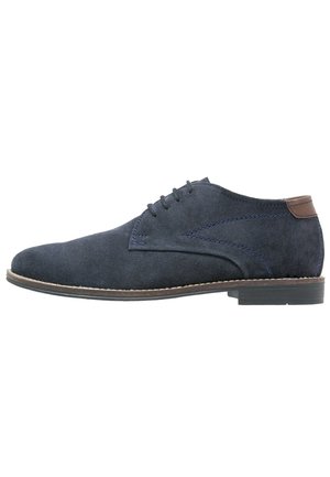 Navy suede oxford schoen met een slanke vorm, bruine leren accenten, vijf veterogen en een contrasterende bruine zool. Gestructureerd oppervlak.