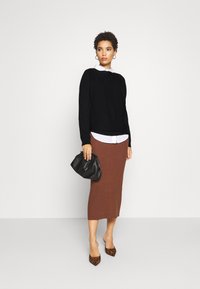 Zwarte trui over een witte blouse, bruine geribbelde midi-rok, met een zwarte clutch en dierenprint hakken.