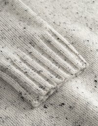 Pull en maille crème avec des taches noires ; présente des poignets côtelés et une texture douce. Gros plan sur le détail de la manche mettant en valeur le motif en tricot.