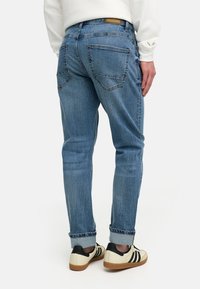 Lys blå denim jeans med en tapered fit, med baklommer og oppbrettede mansjetter. Kombinert med crèmefargede sneakers og en hvit sweatshirt.