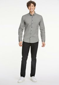 Camisa de botones gris con patrón y botones azules, combinada con pantalones negros y zapatillas blancas. Tejido suave y diseño ajustado.