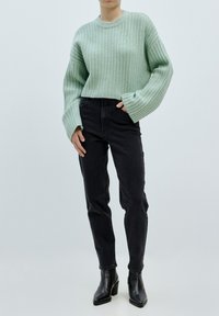 Mintově zelený žebrovaný svetr s objemnými rukávy, zkombinovaný s černými džínami s vysokým pasem a černými kotníkovými botami na podpatku.