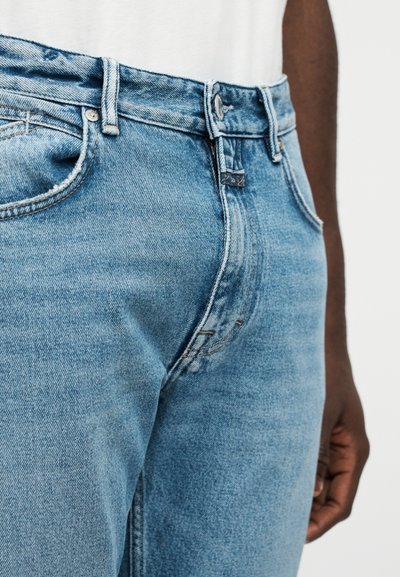 Φωτεινό γαλάζιο τζιν μεσαίας μέσης, σχεδίαση με πέντε τσέπες, ορατή ραφή και κούμπωμα με κουμπί. Μαλακή, ελαφρώς φθαρμένη υφή.