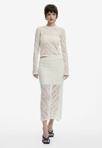 Completo in due pezzi bianco in crocheted, composto da un top a maniche lunghe e una gonna midi, entrambi con intricati motivi a foglia e design a trafori.