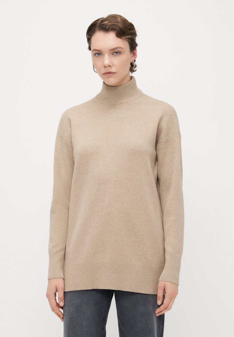 Beige turtleneck genser med løs passform, ribbede mansjetter og kant. Myk tekstur, langstrakt design, minimale sømdetaljer.