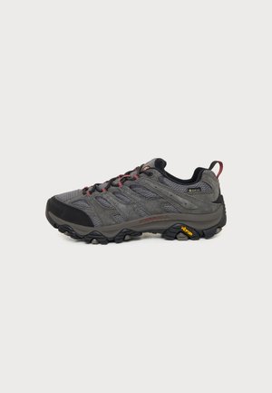 Grijze en zwarte wandelschoen met rode accenten, bovenwerk van mesh en suède, Vibram zool, Gore-Tex label en trekkoordje aan de hiel.