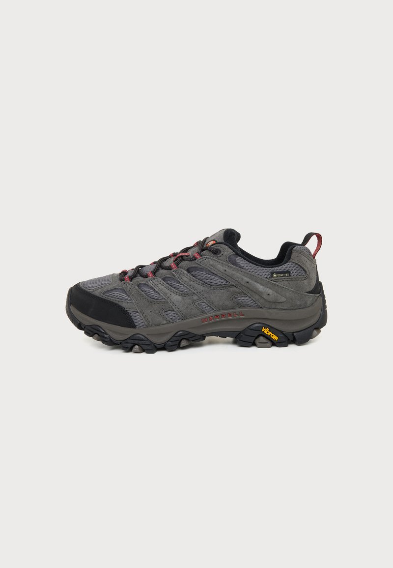 Chaussure de randonnée grise et noire avec des accents rouges, tige en mesh et daim, semelle Vibram, étiquette Gore-Tex et languette au talon.