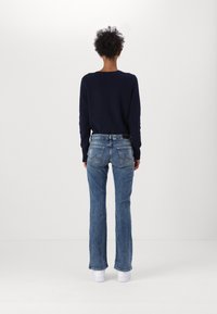 Marineblauer Strickpullover kombiniert mit hellblauen, ausgestellt geschnittenen Jeans, die ein klassisches Fünf-Taschen-Design und dezente Ausbleichungen aufweisen, dazu weiße Sneakers.