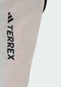 Vaaleanharmaa tekstiili, jossa on sileä pinta, ja sivulla mustalla brodeerattu "TERREX" -brändi. Suunnittelu on virtaviivainen ja toiminnallinen.