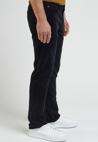 Svarta kordfloddsbyxor med slim fit och subtil textur. Kombineras med vita sneakers med en slät yta och platta snören.