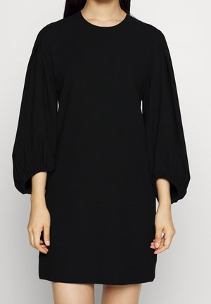 Robe noire avec un col rond, des manches bouffantes de trois-quarts et une coupe ample. Fabriquée en tissu lisse sans motifs ni accents visibles.