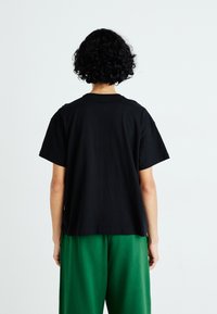 Zwarte katoenen t-shirt met korte mouwen, relaxte pasvorm en ronde hals, gecombineerd met groene losse broek.