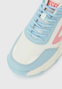 Ανοιχτό μπλε αθλητικό παπούτσι με επάνω μέρος από λευκό καμβά, διακοσμημένο με ροζ γκλίτερ λεπτομέρειες στο λογότυπο και κορδόνια που ταιριάζουν. Στρογγυλερή μύτη με υφή λεπτομερειών.