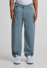Pantalones de pana azul claro con un corte relajado, que cuentan con bolsillos laterales y un pequeño logotipo amarillo en la parte delantera. Diseño texturizado de pierna ancha.