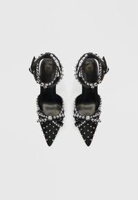 Melni papēži ar smailu purngalu, sudraba kniedēm un kristāliem. Regulējams potītes siksniņa un loksnes detaļa uz purngala. Gluda tekstūra.