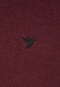Bordeaux gebreide trui met een kleine zwarte geborduurde kolibrie op de borst. Zachte textuur en ribbelstof overal.