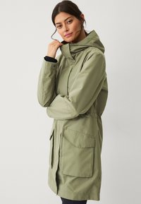 Olijfgroene waterdichte jas met een capuchon, zijzakken en een trekkoord in de taille; gladde textuur en middellang ontwerp.