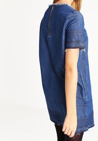 Robe en denim à manches courtes, avec des ourlets effilochés et une fermeture éclair devant. Couleur bleu foncé, coupe décontractée et poches latérales.