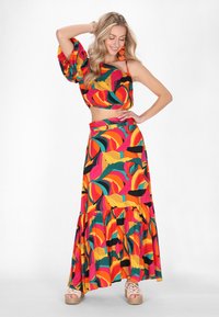 Buntes Zweiteiler-Outfit mit einem verkürzten Oberteil mit Puffärmeln und einem langen Rock, beide in kräftigen Mustern aus Rot, Gelb und Grün.
