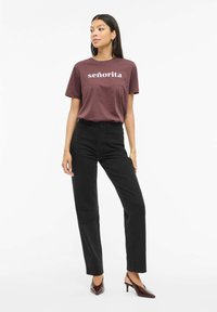 Bordowa bawełniana koszulka z napisem "señorita" w kolorze białym, zestawiona z czarnymi, wysokim stanem dżinsami. Modelka nosi bordowe buty na obcasie z ostrym noskiem.