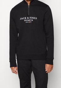 Czarna bluza z suwakiem na ćwierć, z białym napisem "JACK & JONES PREMIUM". Wykonana z miękkiego materiału z ściągaczami przy mankietach i u dołu.