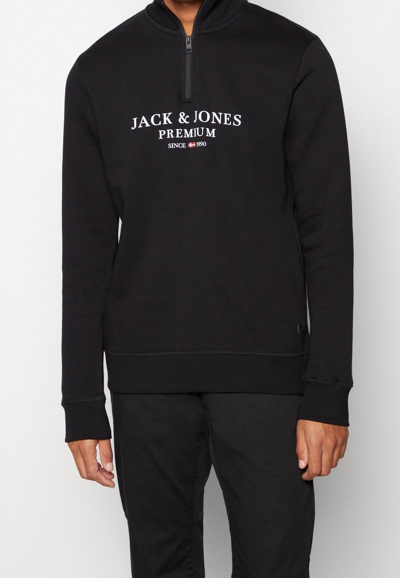 Czarna bluza z suwakiem na ćwierć, z białym napisem "JACK & JONES PREMIUM". Wykonana z miękkiego materiału z ściągaczami przy mankietach i u dołu.