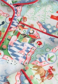 Flanellipyjaman yläosa, jossa on värikkäitä lomateemaisia kuvioita, punainen reuna ja läpällinen tasku erilaisten motiivien kanssa vaaleanvihreällä taustalla.