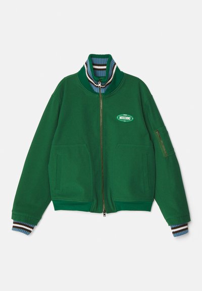 Zelená zapínacia bunda vyrobená z mäkkej tkaniny, s vysokým golierom a pruhovanými akcentmi, dvoma prednými vreckami a značkovou nášivkou.