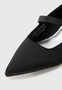 Zapato Mary Jane de satén negro con punta afilada, una tira delgada en el tobillo y un forro metálico plateado. Presenta una plantilla con marca que incluye detalles de tamaño.